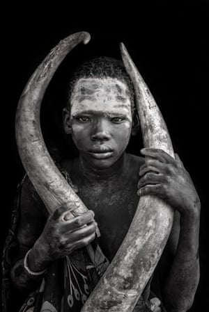 A young South Sudanese boy with his forehead painted holding two cattle horns