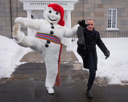 Bonhomme Carnaval, novelty snowman mascot of the Quebec Winter Carnival, in a red woolly hat and a multicoloured sash across his waste, and Canadian PM Mark Carney, dressed in dark suit and long dark coat, do high-kicks before the Citadelle in Quebec City