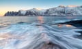 The waves of the icy sea crashing on the rocky cliffs at dawn, Tungeneset, Troms county, Norway.
