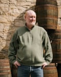 A man with his hands on his hips, standing in front of stacked whisky barrels