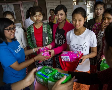 A woman in a blue Unicef T-shirt hands sanitary products to a group of young women