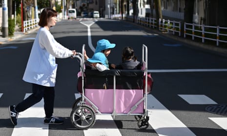 Children from a nursery school travel in a pram along a street in Tokyo