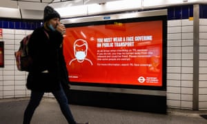 A woman walks past a sign reminding commuters to wear a face covering on public transport at Leicester Square Station in London.