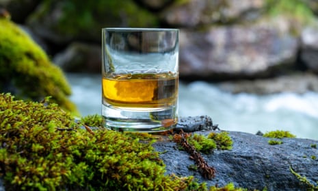 A glass of whisky on a mossy rock by a fast-flowing beck.