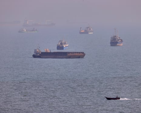 A small boat sails past cargo ships and other commercial vessels