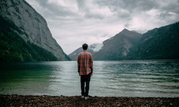 A man standing at the shore of a mountain lake, looking across it