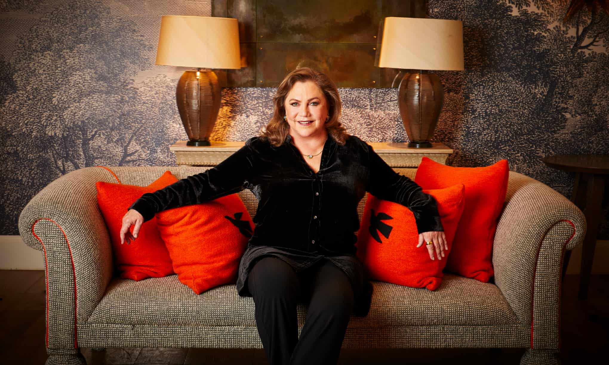 Kathleen Turner on a grey couch with red cushions