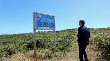 A man looks at a sign on a hillside that says ‘demain, ici, futur de village’ (Tomorrow, here the future of the village)