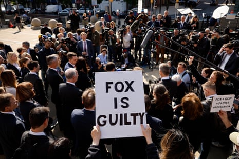 A large group of people are gathered, one person is holding a sign that reads 'Fox is guilty'.