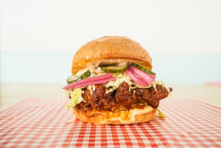 A spicy fried chicken burger with coleslaw, pickles and pickled onions on a checked cloth
