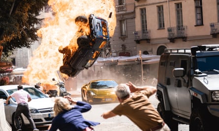 People cower as an exploding car is propelled into the air