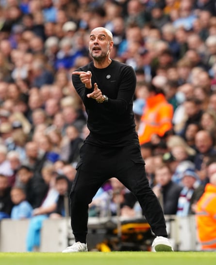 Pep Guardiola on the sideline of the pitch, dressed in black combat-style trousers with white trainers