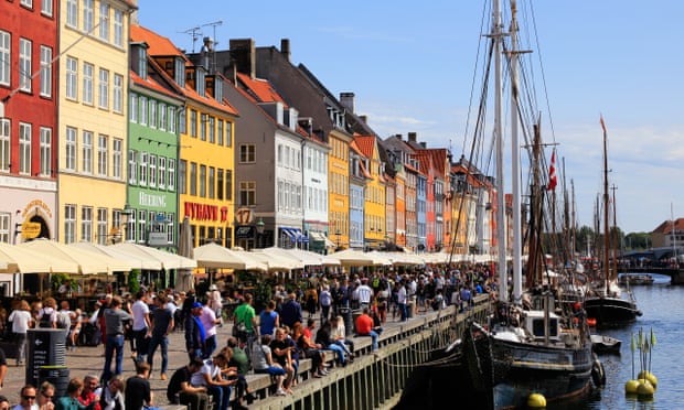 View of the Nyhavn area of Copenhagen with multi-coloured buildings, the canopies of restaurants lining the canal and crowds of people