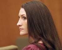 Woman with long brown hair and red top sits expressionless in profile in a courtroom.
