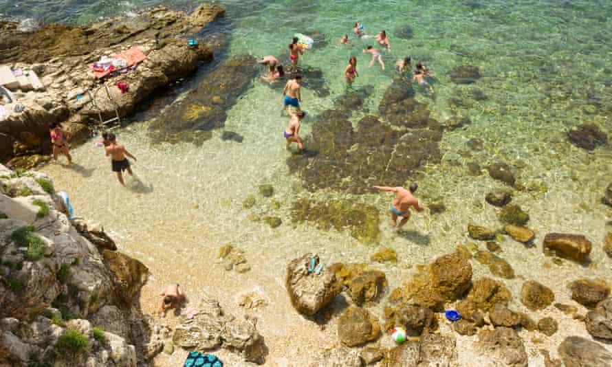 A high angle view of people swimming in the shoal and sunbathing on the rocks of the city beach in Rovinj, Croatia