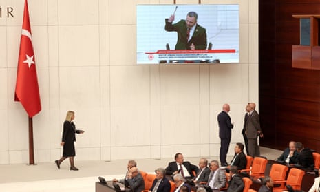 Lawmaker Buray Erbay (on screen), who protested against the proposed law during a speech to the Turkish Grand National Assembly, symbolically smashing his own phone with a hammer