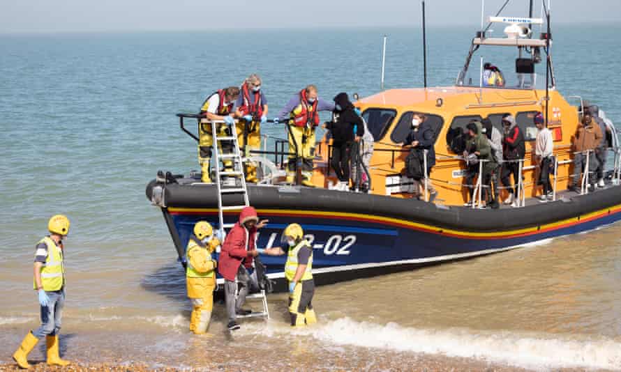 An RNLI lifeboat helps migrants ashore on Dungeness beach, Kent, as onlookers shout “traitor” at the crew.