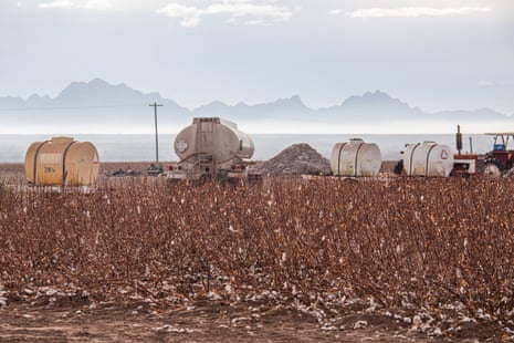 field with agricultural equipment, including containers and vehicles, and mountains in the background