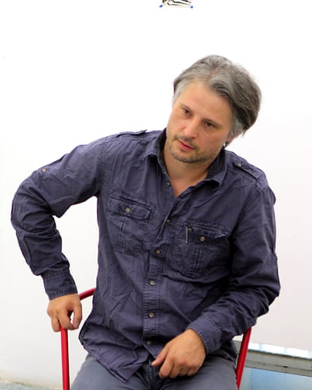 Sebastian Bieniek in a blue shirt and jeans, sitting on a director's chair