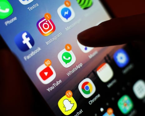 A thumb hovers over many app icons displayed on the glowing screen of a smartphone.