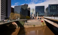 A low and brown-looking river flowing underneath two bridges, with office buildings or blocks of flats in the background