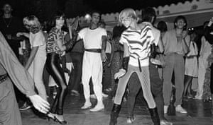 Black-and-white photo of a group of people dancing on a dancefloor, one in a tiger-print top, stripy skinny trousers and boots, and another in leather trousers