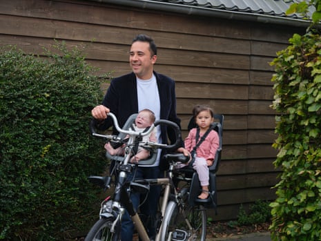 Enrique Alvarez stands next to a bike with his youngest daughter, Alaia Belen, in the bike’s backseat and his self-made reborn doll, Rainbow Yoshi, in the front