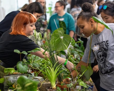 two young women lean across a long table with lots of pots of different types of houseplant