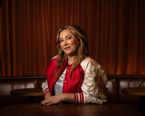 Ella Hooper rests her arms on a table, smiling gently, wearing a beaded red and white jacket