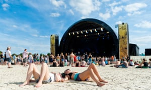 Revellers lie on the sand in front of a festival music stage at A Summer’s Tale, Germany