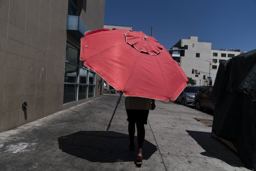 A woman walks on the sidewalk with a large pink umbrella.