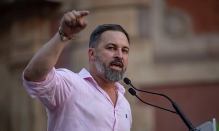 Santiago Abascal indossa una maglietta con il collo aperto e gesticola mentre parla al microfono