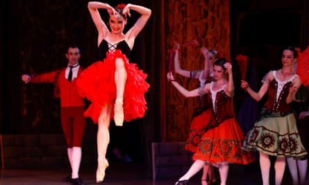 A ballerina in red tutu leaping on stage, with chorus in background