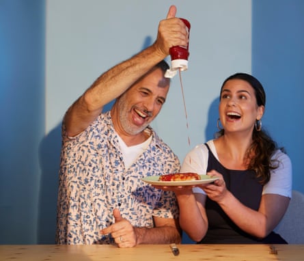 Yotam Ottolenghi squeezing ketchup on to a plate of baked beans held by Noor Murad