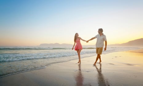 Couple, holding hands, walking along sunny beach.
