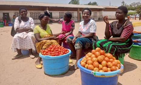 Five women sit talking next to buckets of tomatoes in a large open area