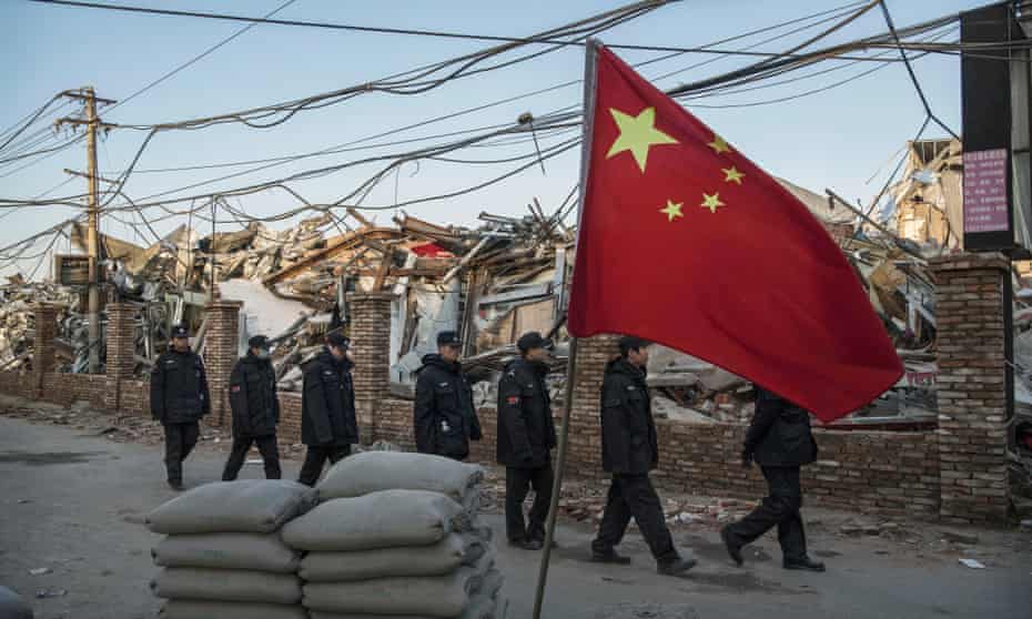 Chinese police walk in a line passed buildings demolished by authorities in an area that used to have migrant housing and factories. Rare protests have broken out in Beijing over the evictions.