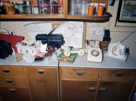 A telephone left off the hook on a dark brown cabinet with a shelf of drinks and drinking glasses behind it.