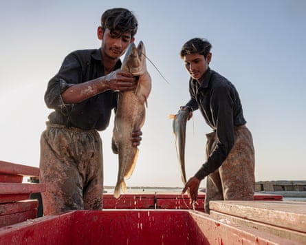 Two young men hold fish above red plastic containers