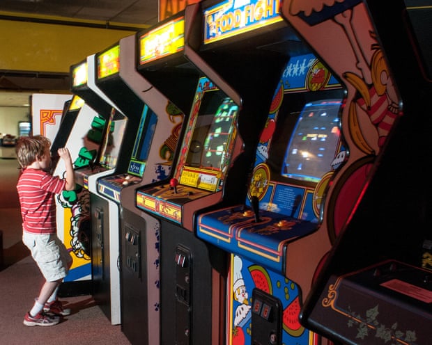 A boy reaches up to a glowing arcade machine in a row of retro video game cabinets
