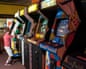 A boy reaches up to a glowing arcade machine in a row of retro video game cabinets