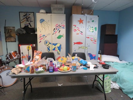 A makeshift bed sits in the corner of the WKCR break room, next to a table full of snacks. in the background are cabinets with brightly colored decorations showing fish and a cow in a space helmet