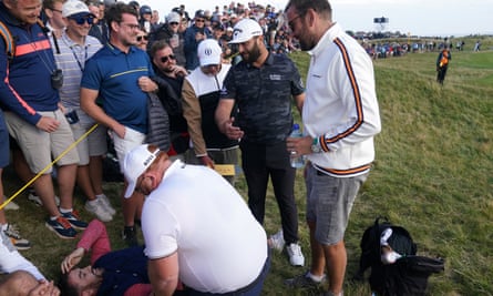 Jon Rahm memeriksa kipas angin, tergeletak di tanah di belakang tali penonton dan dijaga, yang secara tidak sengaja dia pukul dengan pukulan tee di Open.