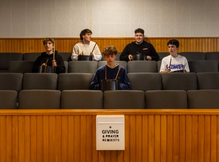The drummers sitting with space between them on audience seating in a theatre