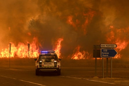 Officers in a police car monitor a wildfire nearing a road junction