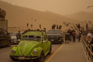 People walk on a hillside in murky yellow light with cars parked in the foreground