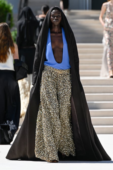 A model at Balenciaga wearing wide leopard-print trousers, a blue deep cut halterneck and a hooded gown.