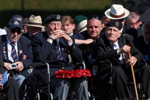War veterans sit in a line with medals, ties, hats, some in wheelchairs and with sticks