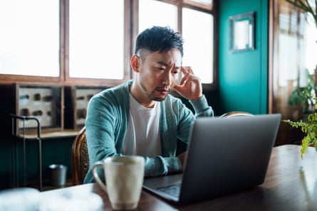 man frowns while looking at a laptop screen in what looks like a coffeeshop