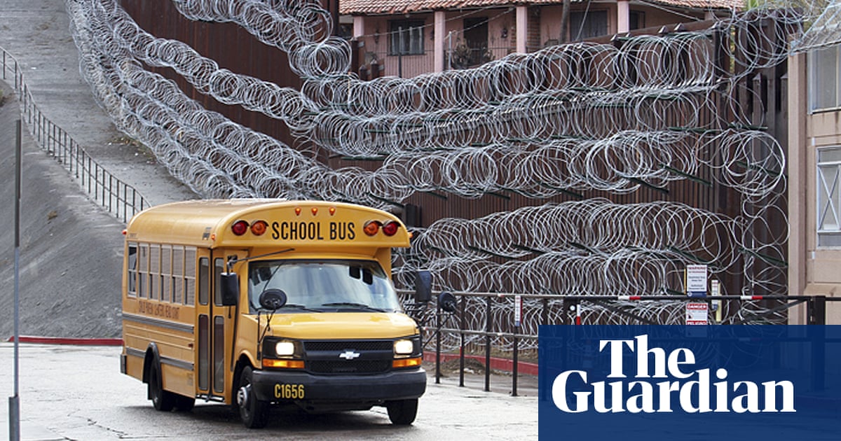 Photo of schoolbus driving past a wall with six rows of concertina razor wire attached to it